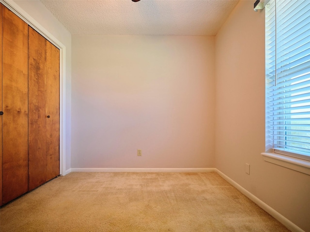 unfurnished bedroom with light colored carpet, a textured ceiling, and a closet