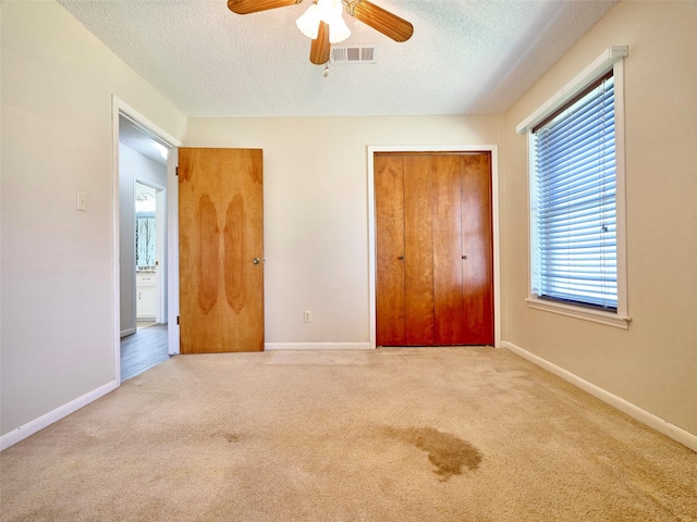 unfurnished bedroom with ceiling fan, light colored carpet, a textured ceiling, and a closet