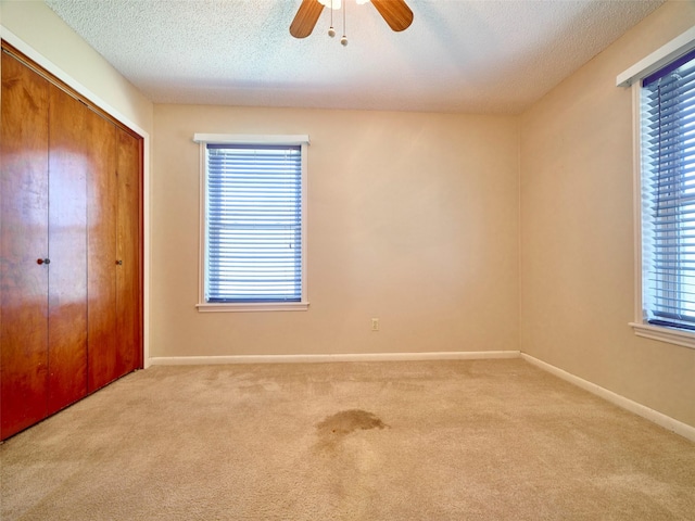 unfurnished bedroom with ceiling fan, light colored carpet, a closet, and a textured ceiling