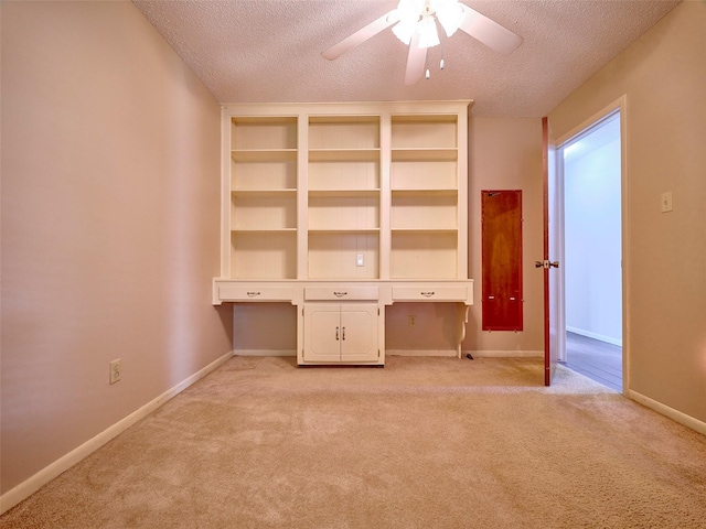 interior space with ceiling fan, built in desk, light carpet, and a textured ceiling