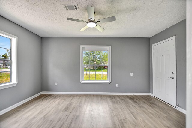 empty room with a textured ceiling, wood-type flooring, and a wealth of natural light