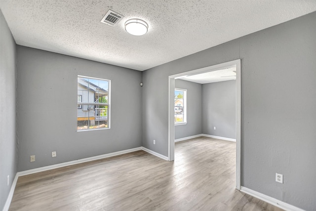 empty room featuring a textured ceiling, plenty of natural light, and light hardwood / wood-style flooring