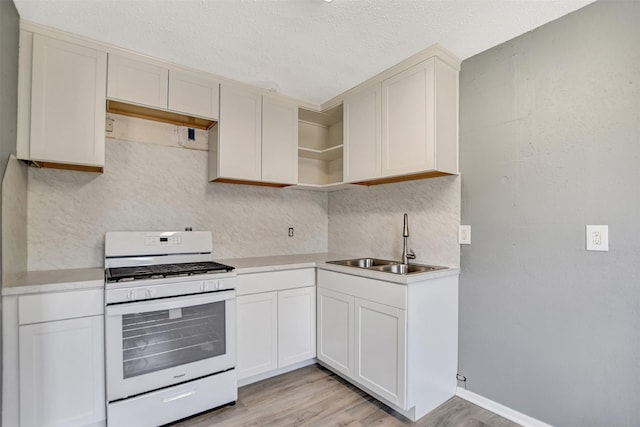 kitchen featuring sink, backsplash, light hardwood / wood-style floors, white gas range oven, and white cabinets