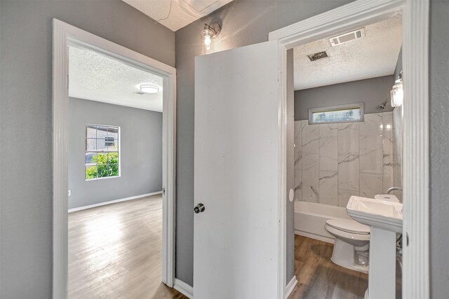 bathroom featuring a textured ceiling, toilet, hardwood / wood-style floors, and tiled shower / bath