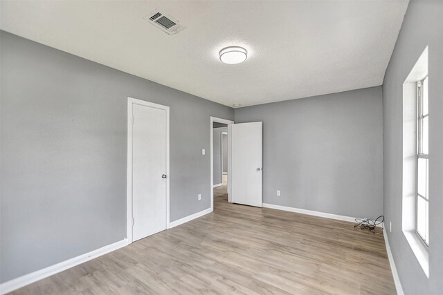 spare room featuring light hardwood / wood-style flooring, a wealth of natural light, and a textured ceiling