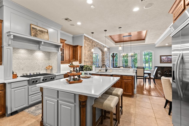 kitchen with tasteful backsplash, light wood-type flooring, a raised ceiling, a kitchen island, and decorative light fixtures