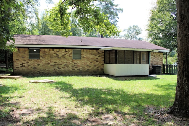 back of house featuring a lawn, a sunroom, and an outdoor fire pit