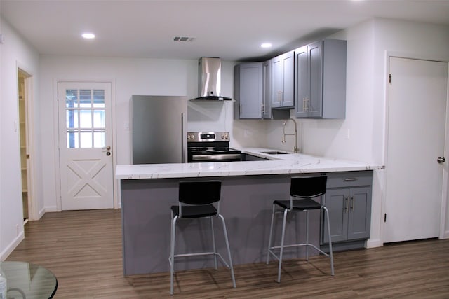 kitchen with gray cabinets, wall chimney range hood, kitchen peninsula, and stainless steel appliances