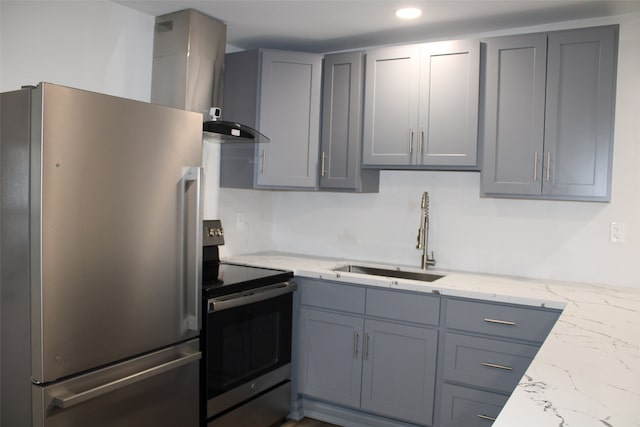 kitchen with gray cabinetry, wall chimney range hood, appliances with stainless steel finishes, light stone countertops, and sink