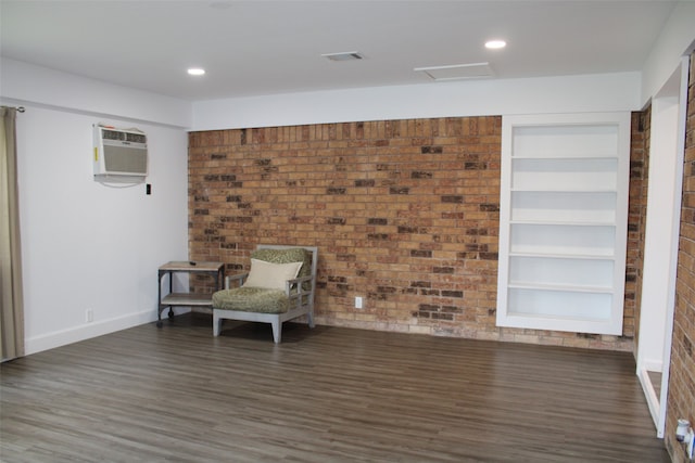 unfurnished room featuring dark wood-type flooring, built in features, brick wall, and an AC wall unit