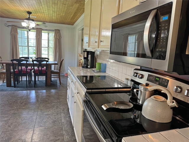 kitchen featuring tile countertops, wooden ceiling, crown molding, decorative backsplash, and stainless steel appliances