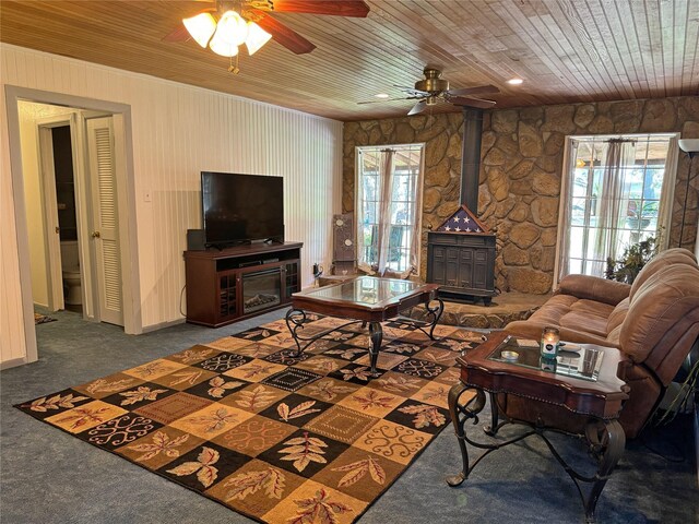 living room with a wood stove, a wealth of natural light, wooden ceiling, and dark colored carpet