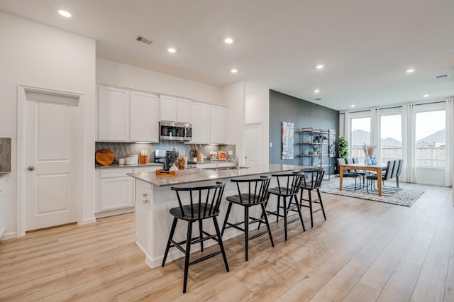 kitchen with stainless steel appliances, a center island with sink, light hardwood / wood-style flooring, white cabinets, and a breakfast bar area