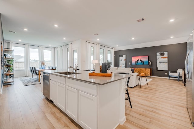 kitchen featuring white cabinets, sink, an island with sink, and light hardwood / wood-style flooring