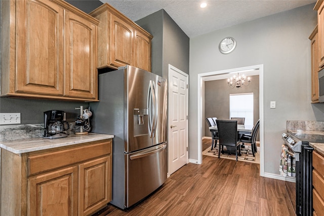 kitchen with appliances with stainless steel finishes, dark wood-type flooring, a textured ceiling, and a notable chandelier