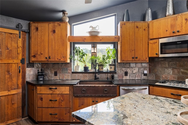 kitchen featuring light stone counters, appliances with stainless steel finishes, a barn door, tasteful backsplash, and sink