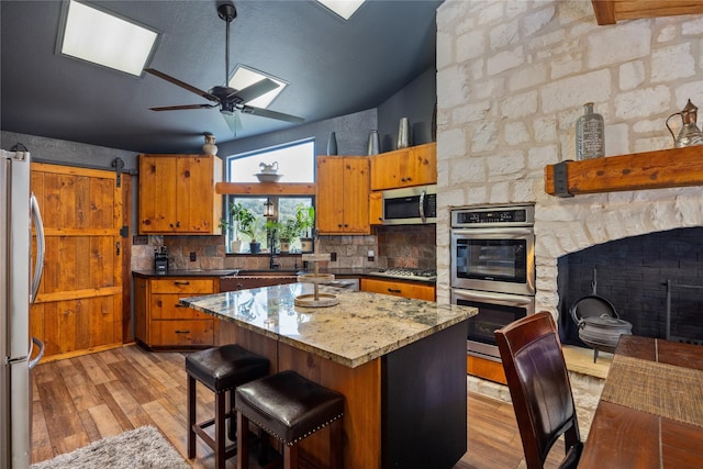 kitchen featuring ceiling fan, stainless steel appliances, a barn door, and light wood-type flooring