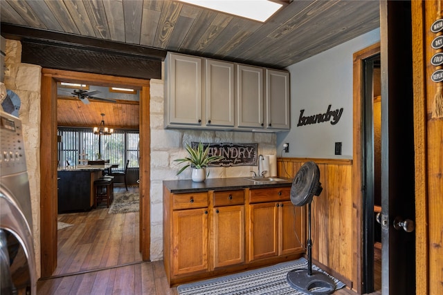 bar featuring ceiling fan with notable chandelier, wooden ceiling, washer / clothes dryer, sink, and wood-type flooring