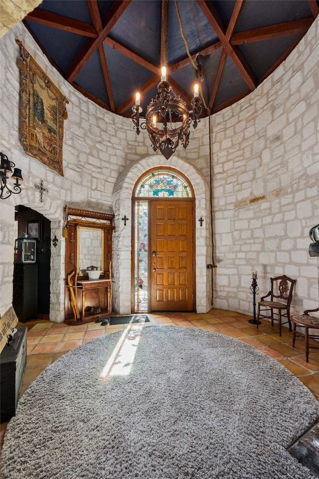 tiled entryway with beam ceiling, a high ceiling, and a chandelier