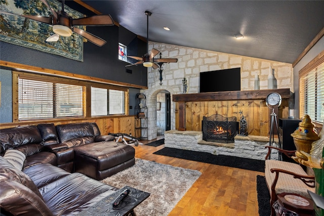 living room with a textured ceiling, ceiling fan, hardwood / wood-style flooring, high vaulted ceiling, and a fireplace