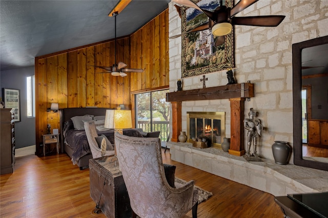 living room featuring high vaulted ceiling, a stone fireplace, wooden walls, ceiling fan, and hardwood / wood-style floors