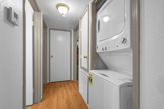 clothes washing area with light wood-type flooring, a textured ceiling, and stacked washing maching and dryer