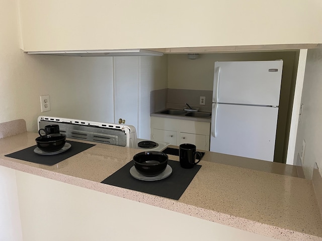 kitchen featuring light stone countertops, sink, and white fridge