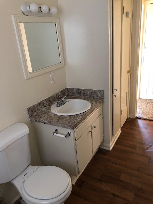 half bath featuring vanity, toilet, and wood finished floors