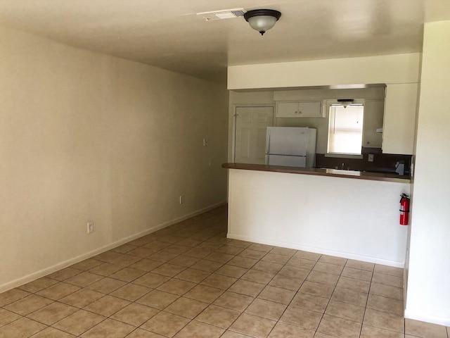 kitchen featuring light tile patterned floors, kitchen peninsula, and white refrigerator