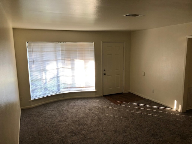 empty room featuring baseboards, visible vents, and dark colored carpet