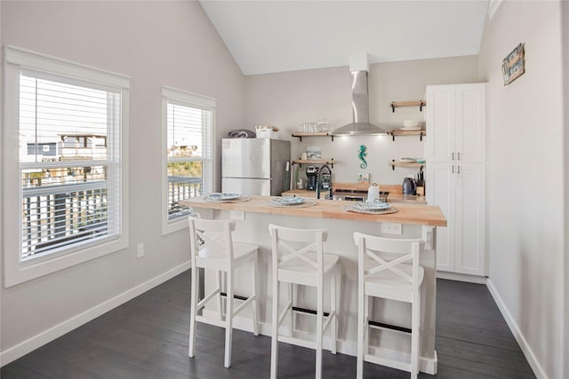 kitchen with a breakfast bar area, exhaust hood, white cabinets, and stainless steel refrigerator