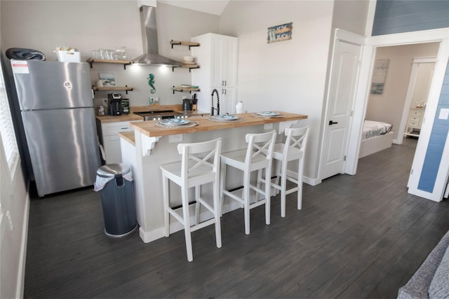 kitchen with extractor fan, wood counters, white cabinetry, stainless steel fridge, and a kitchen bar