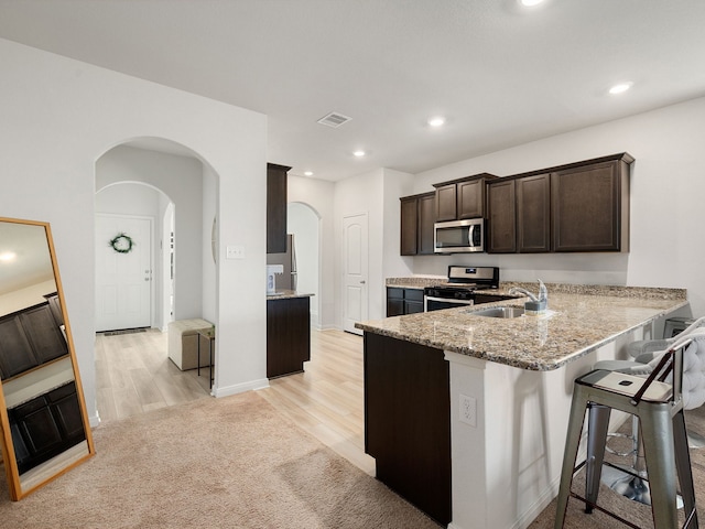 kitchen featuring kitchen peninsula, light stone countertops, a breakfast bar area, appliances with stainless steel finishes, and sink