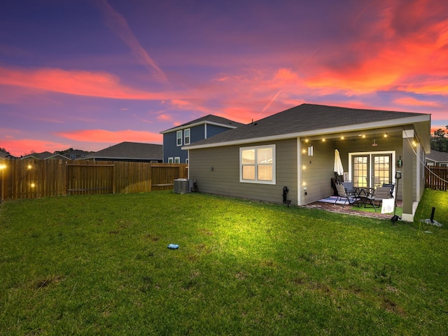 back house at dusk featuring central air condition unit, a patio, and a yard