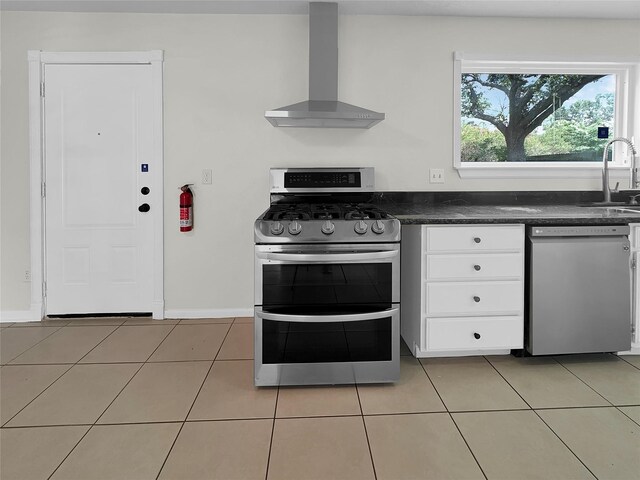 kitchen featuring stainless steel appliances, sink, light tile patterned floors, white cabinets, and wall chimney range hood