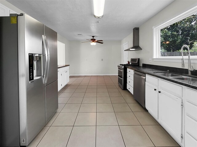 kitchen featuring light tile patterned floors, appliances with stainless steel finishes, ceiling fan, sink, and wall chimney range hood