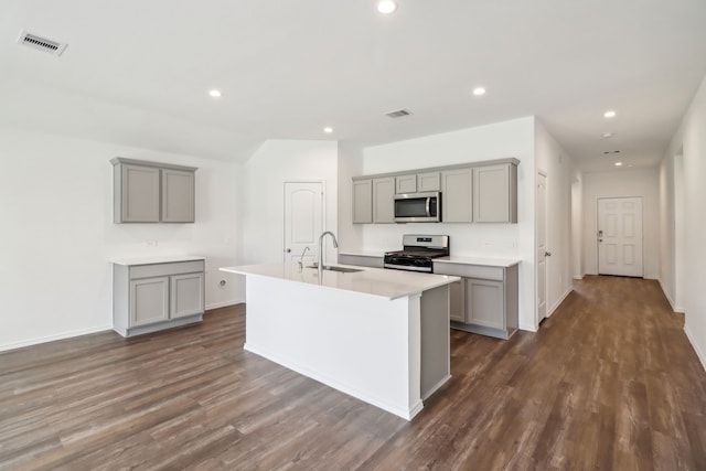 kitchen with gray cabinetry, an island with sink, dark wood-type flooring, and appliances with stainless steel finishes