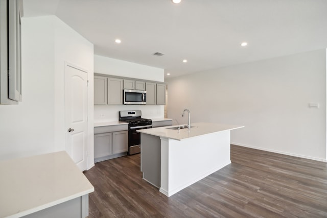 kitchen with gray cabinetry, stainless steel appliances, sink, a center island with sink, and dark hardwood / wood-style floors