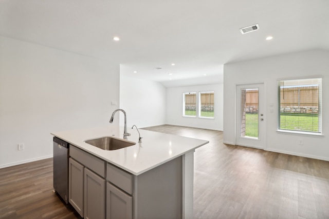 kitchen featuring stainless steel dishwasher, sink, hardwood / wood-style floors, gray cabinets, and an island with sink