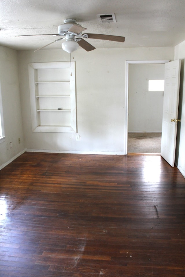 empty room with a textured ceiling, ceiling fan, built in features, and dark hardwood / wood-style flooring