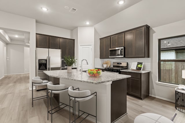 kitchen with a kitchen island with sink, appliances with stainless steel finishes, a kitchen bar, light stone counters, and lofted ceiling