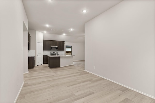 kitchen featuring light hardwood / wood-style flooring, a center island with sink, tasteful backsplash, appliances with stainless steel finishes, and dark brown cabinets