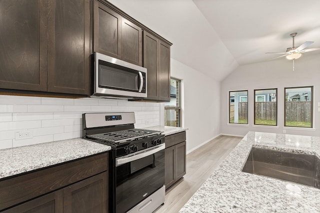 kitchen with lofted ceiling, sink, light stone countertops, and appliances with stainless steel finishes