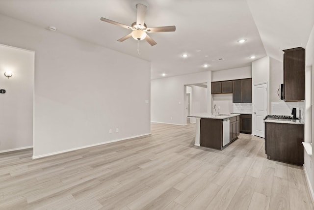 kitchen with an island with sink, light hardwood / wood-style floors, tasteful backsplash, ceiling fan, and sink