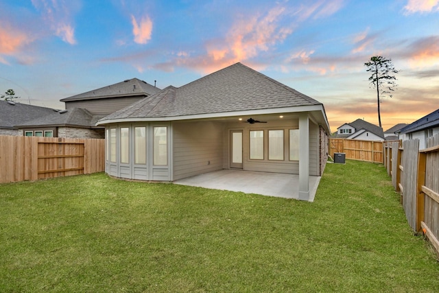 back house at dusk with cooling unit, a patio area, ceiling fan, and a lawn