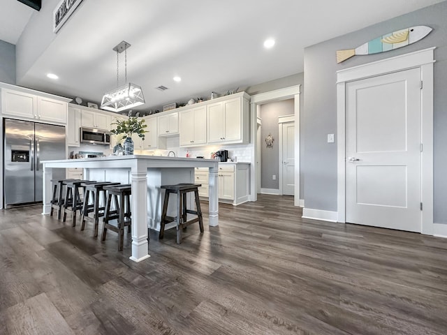 kitchen with dark wood finished floors, white cabinets, stainless steel appliances, and a kitchen bar