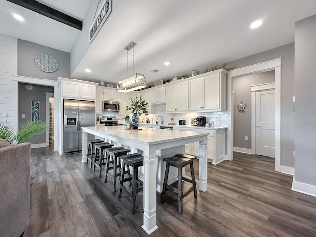 kitchen with a breakfast bar, dark wood-type flooring, appliances with stainless steel finishes, white cabinetry, and tasteful backsplash