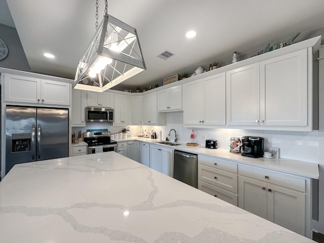 kitchen featuring visible vents, a sink, hanging light fixtures, stainless steel appliances, and backsplash