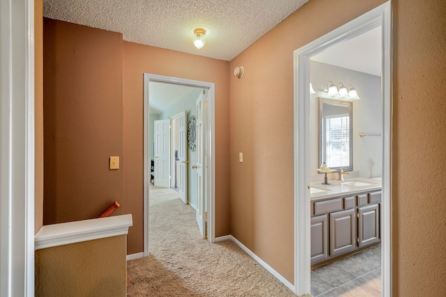 hallway with light carpet, sink, and a textured ceiling