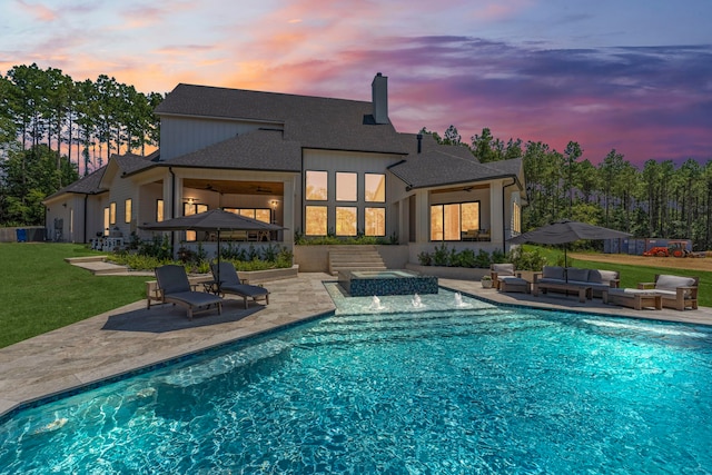 pool at dusk with a yard, a patio, an outdoor living space, and pool water feature